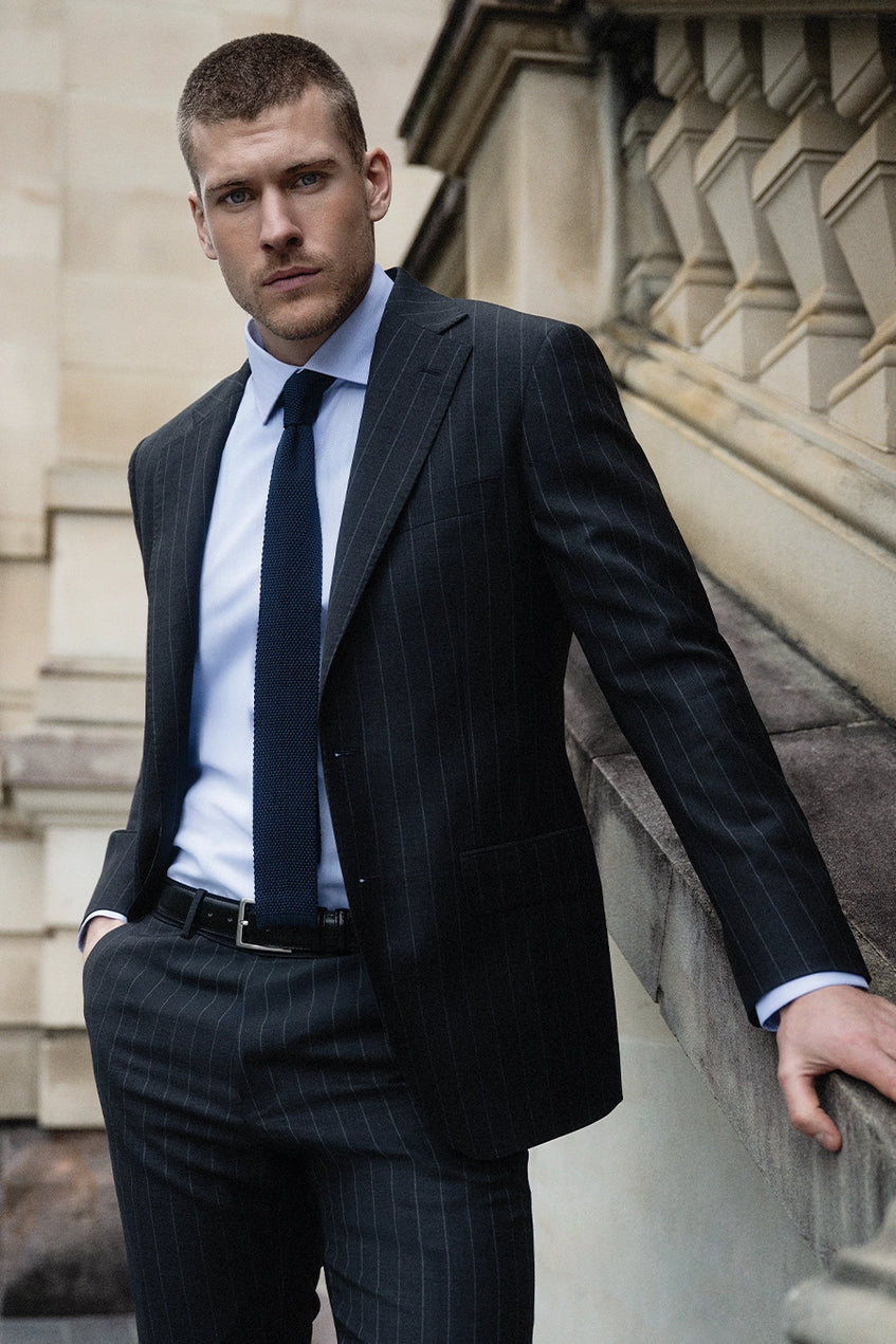 Man wearing suit with light blue shirt holding the wall of a building