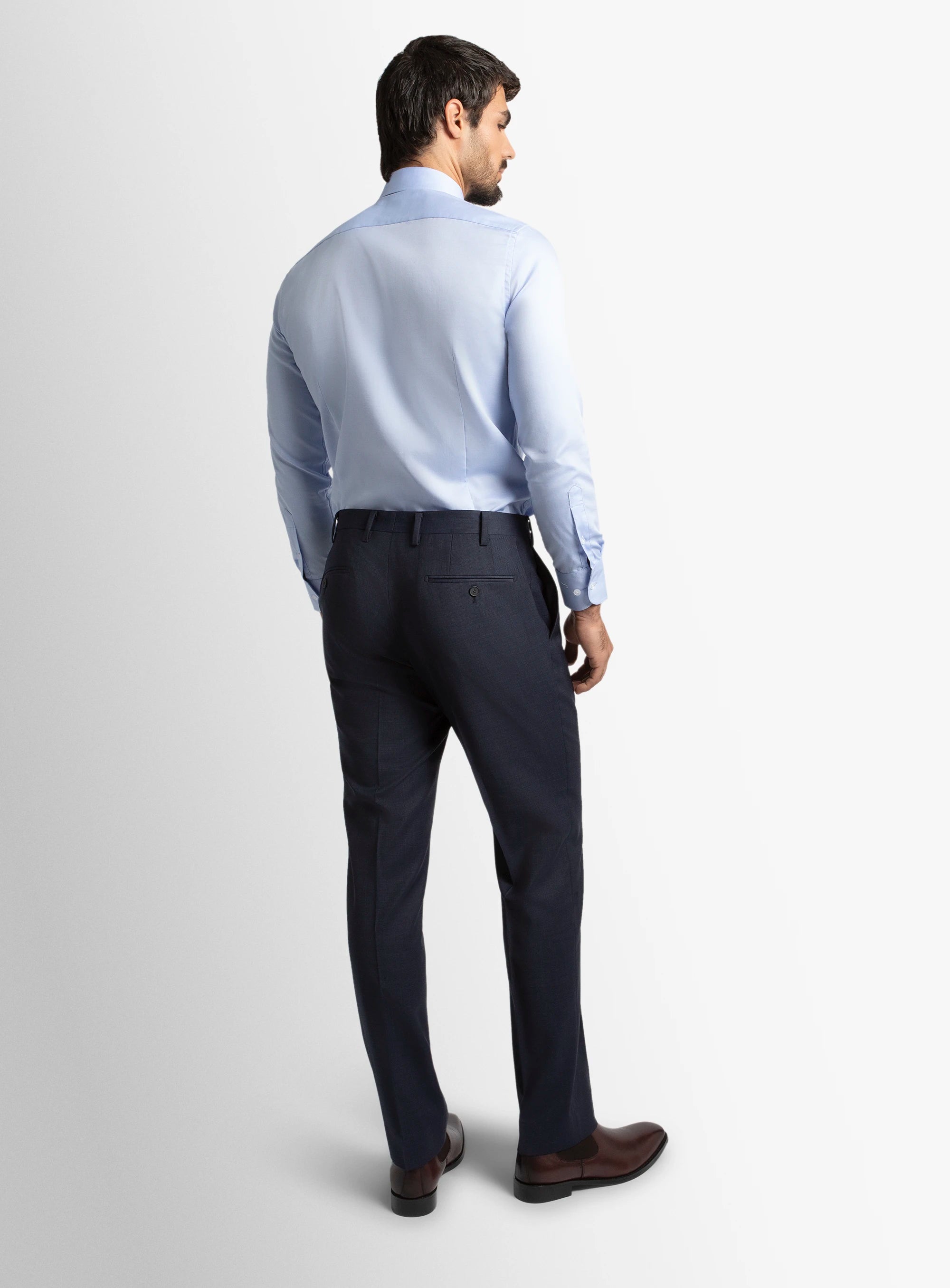 Man wearing a light blue dress shirt and dark pants on a white background