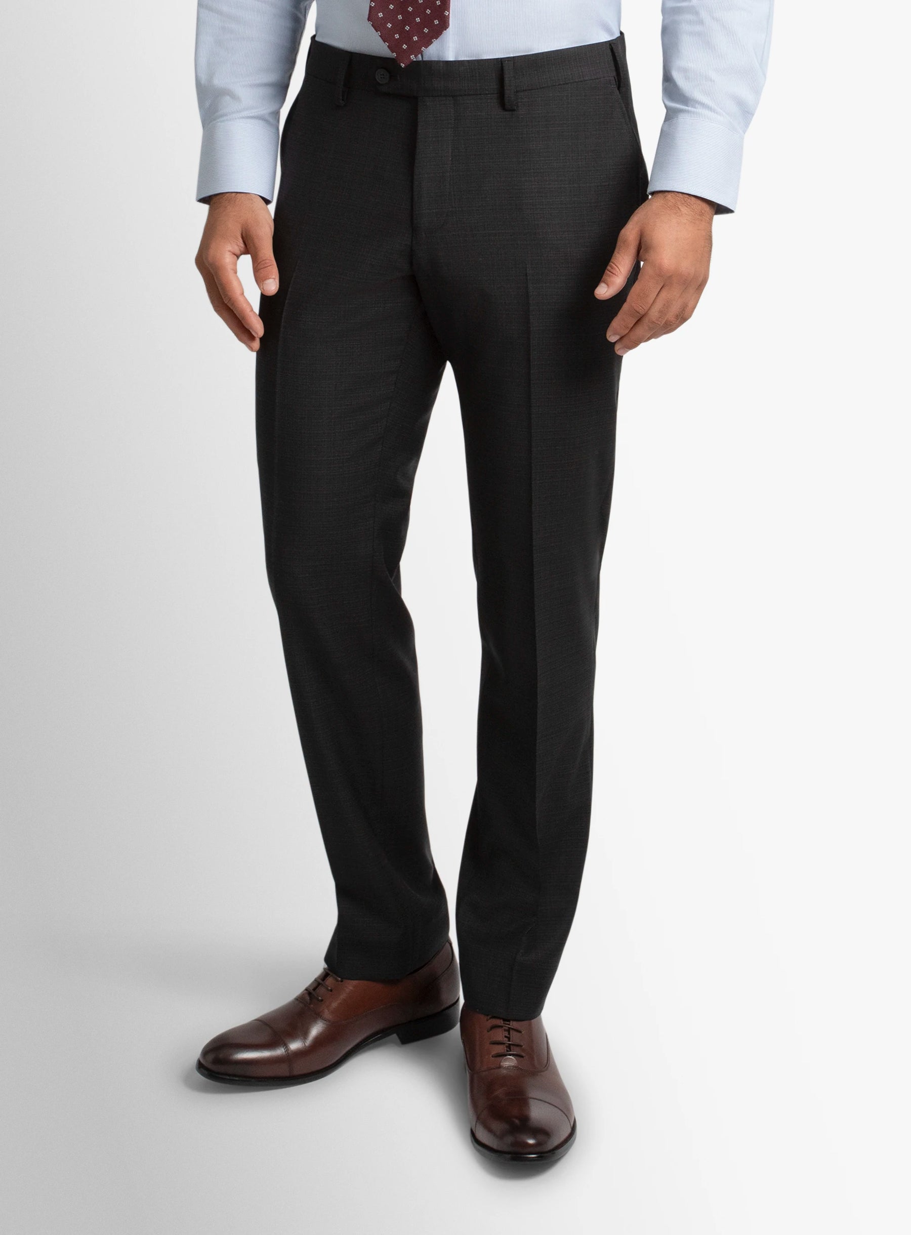 Person wearing dark gray dress pants with a white shirt and brown shoes on a light gray background