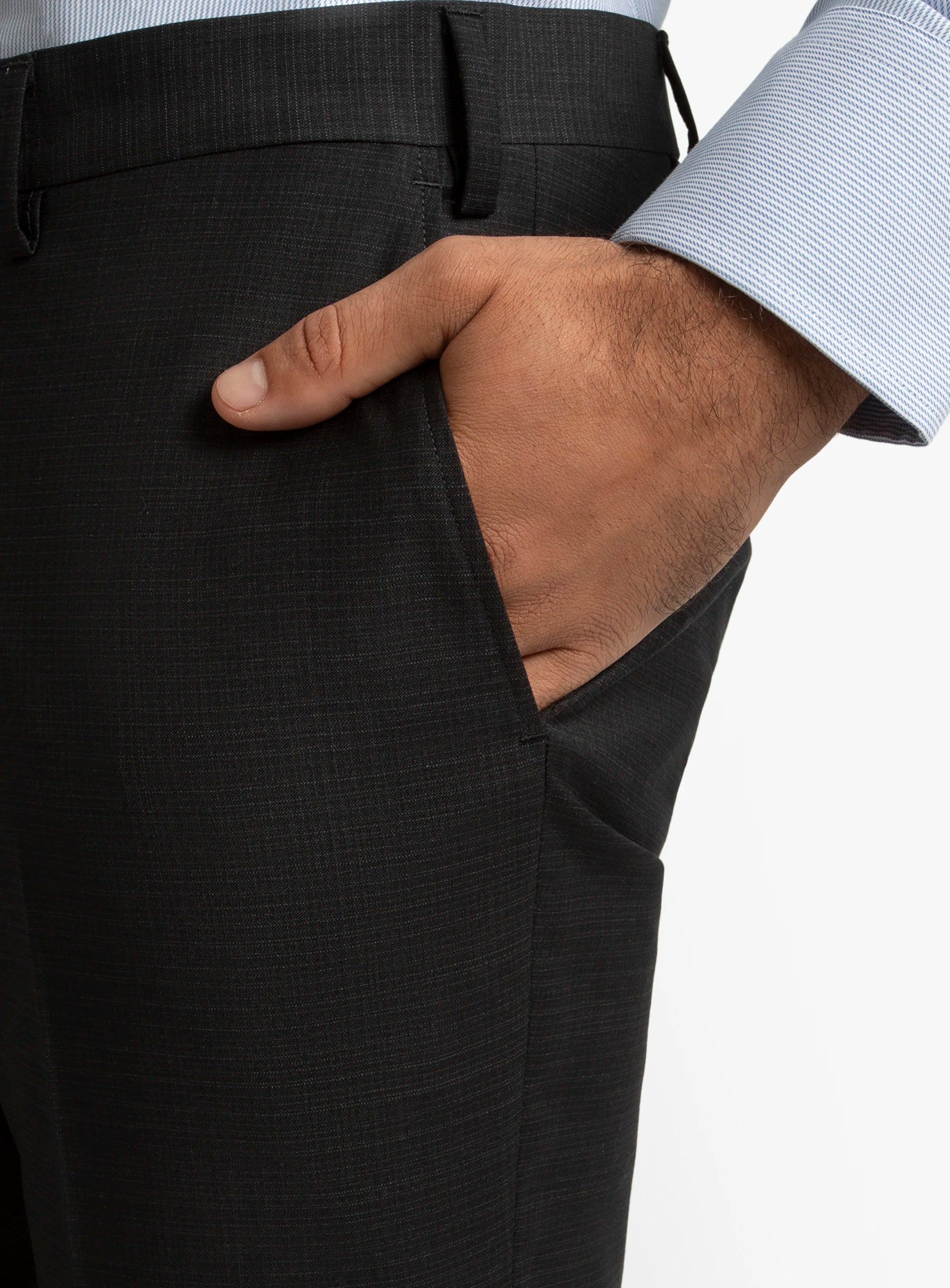 Close-up of a person wearing dark gray pants with a light-colored shirt sleeve.
