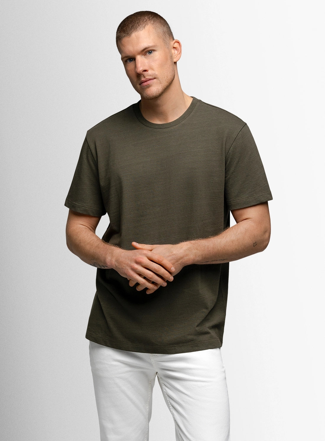 Man wearing a green t-shirt and white pants on a light gray background