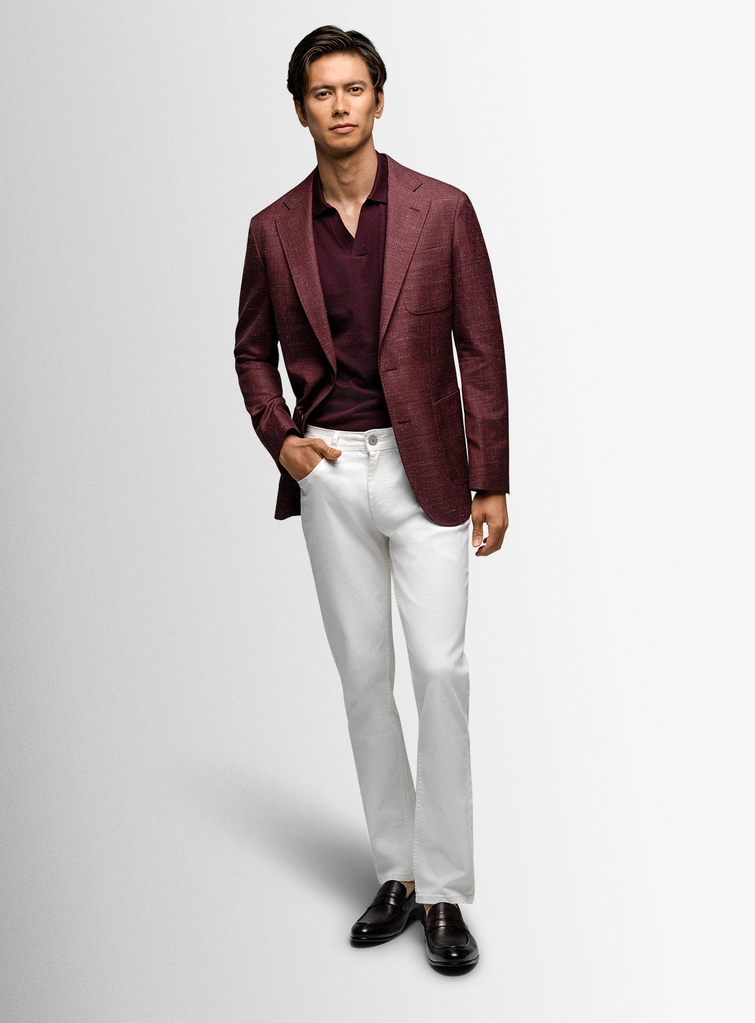 Man wearing a burgundy blazer, white shirt, and white pants on a light gray background