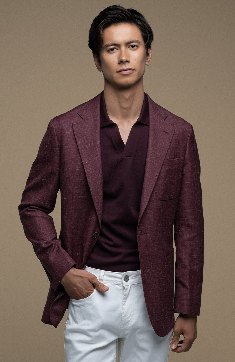 Man wearing a burgundy blazer over a dark shirt with white pants on a beige background