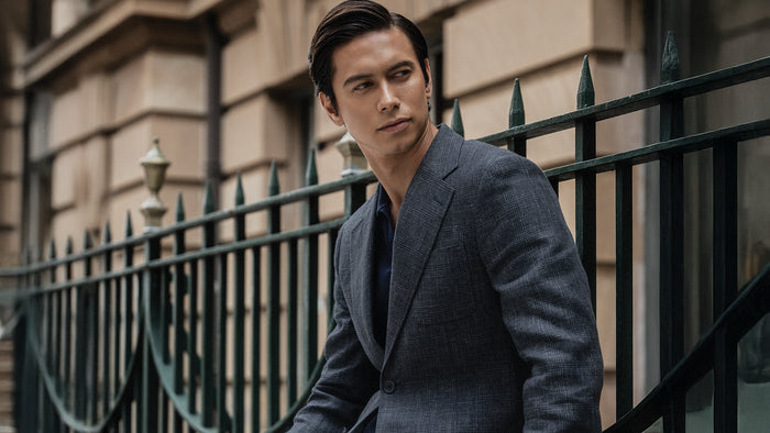 Man in a gray suit standing in front of a black metal gate with a building in the background
