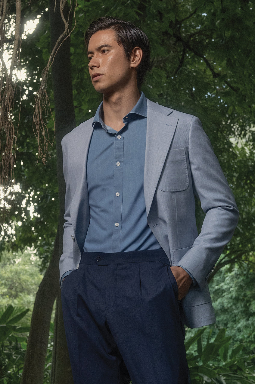 Man in a gray blazer and blue shirt standing in a forest setting