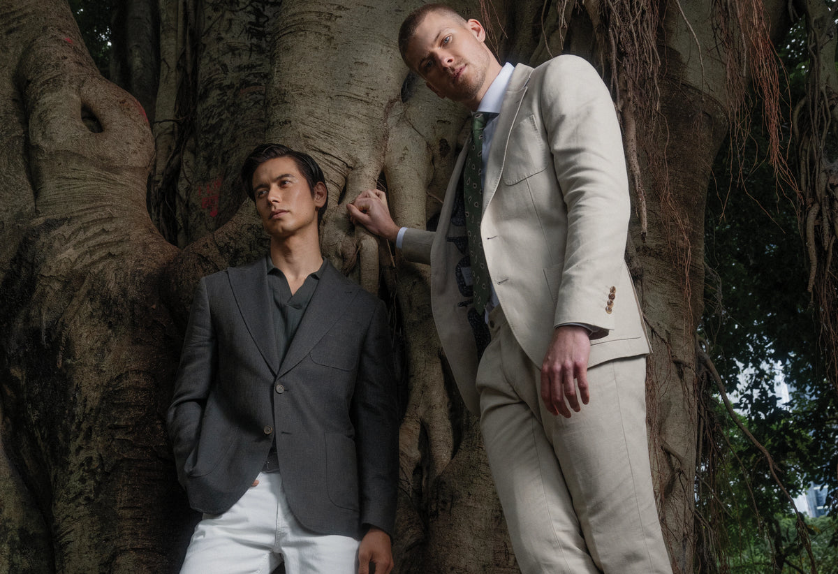 Two men in suits standing in a natural setting with trees.