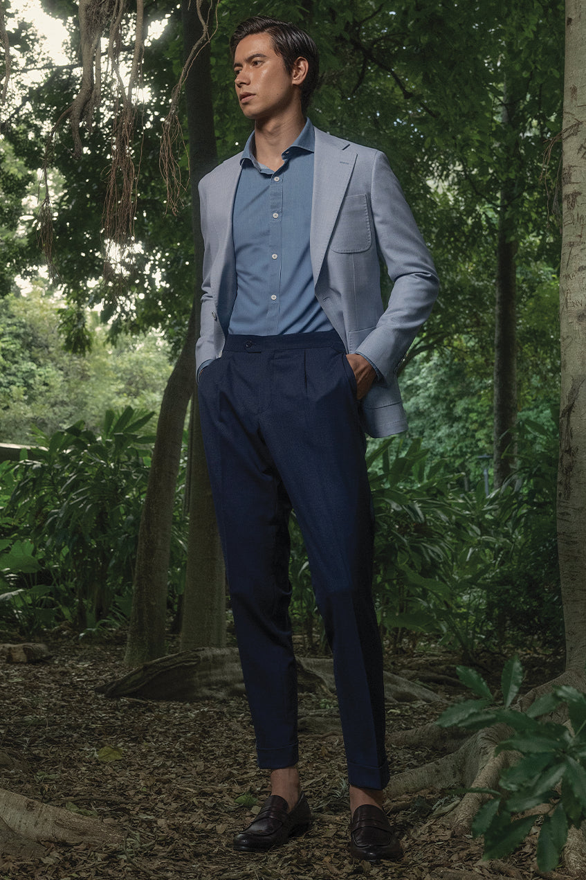 Man in a light gray blazer and blue shirt standing in a forest setting