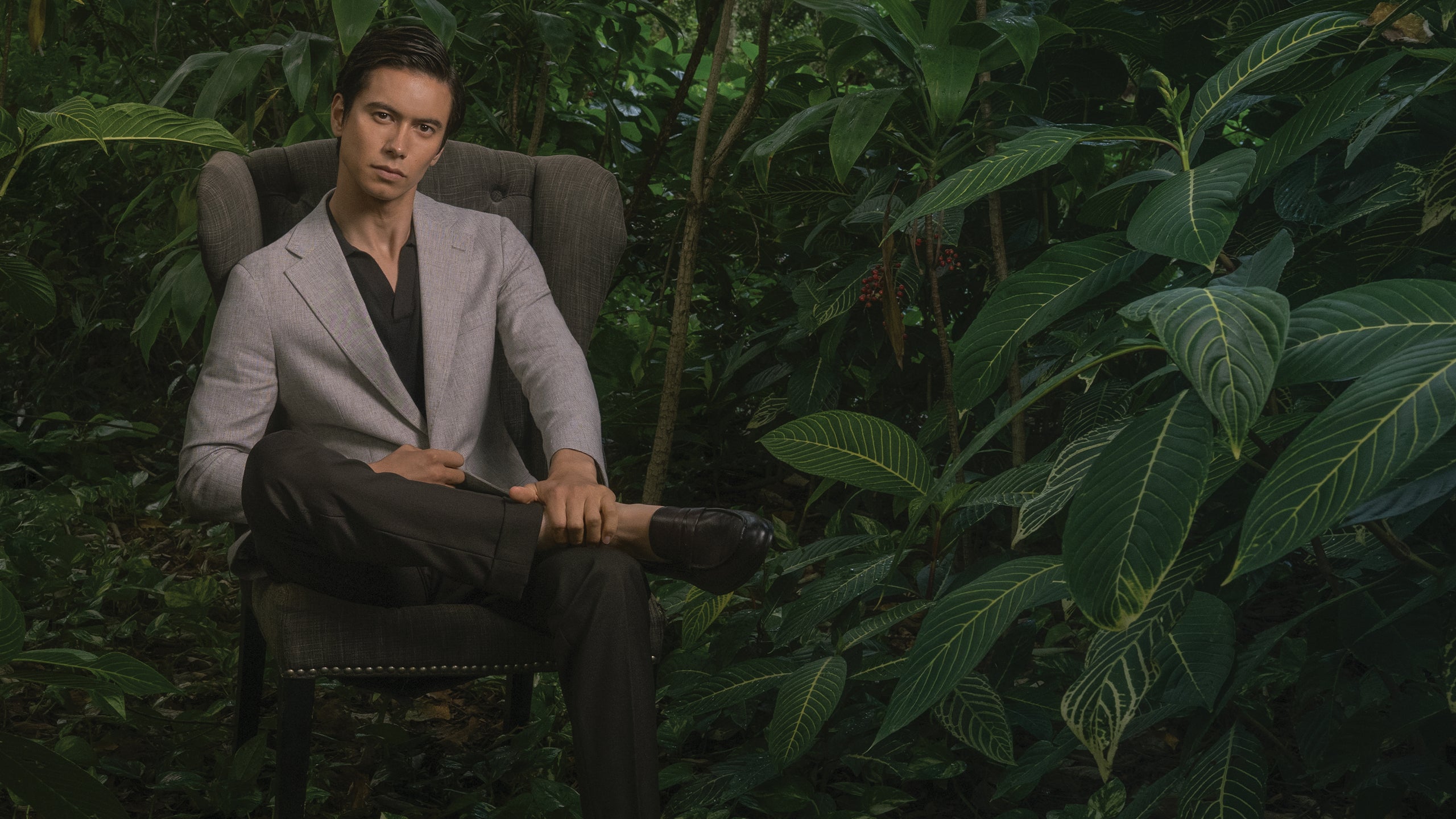 Man sitting in a chair surrounded by green foliage