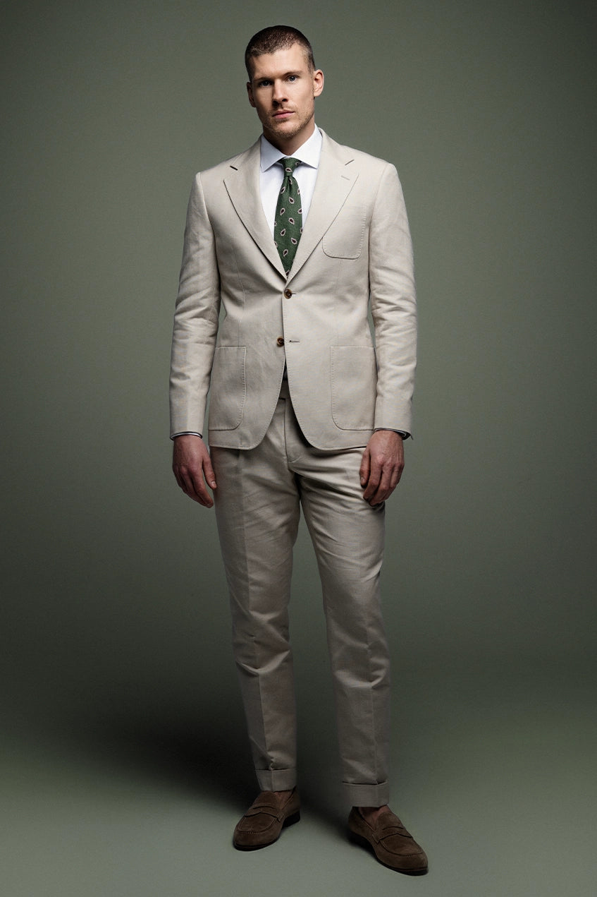 Man wearing a beige suit with a green tie against a gray background