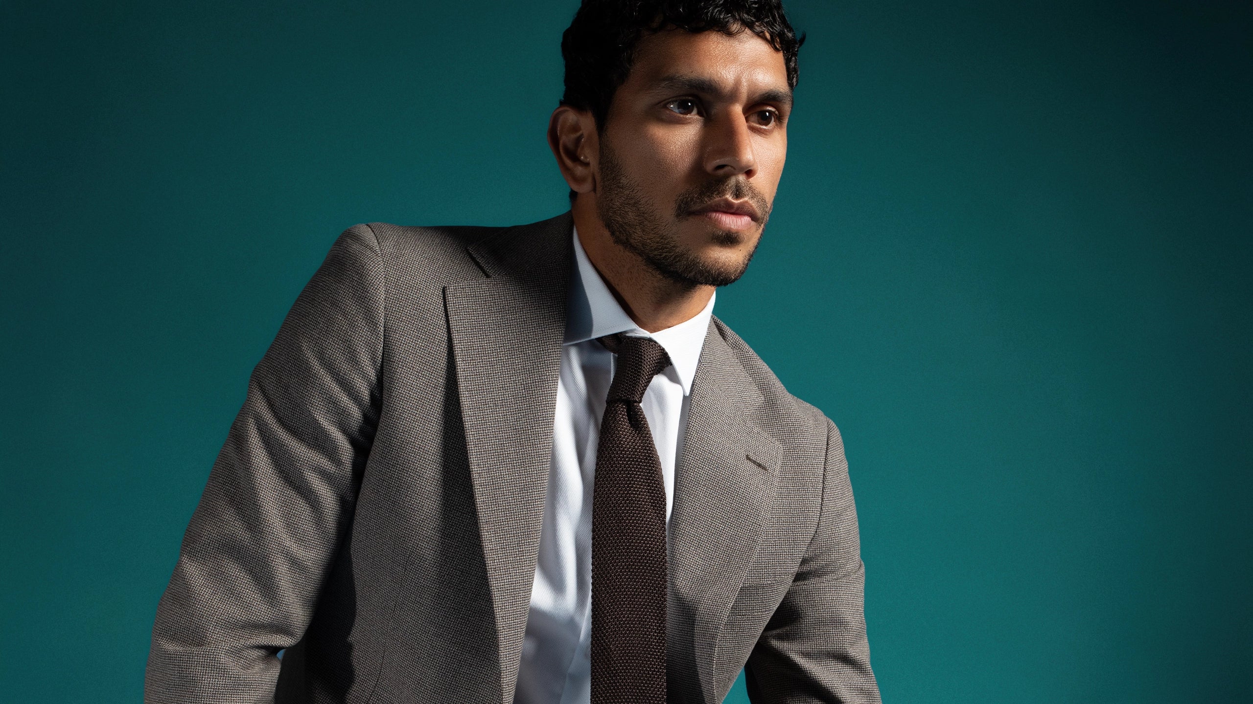 Man wearing a gray suit with a brown tie against a teal background
