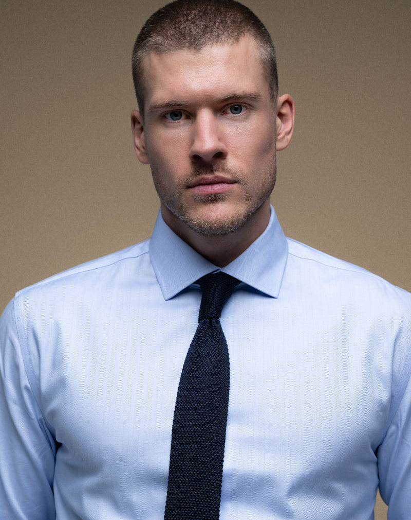 Man wearing a light blue shirt and black tie against a beige background