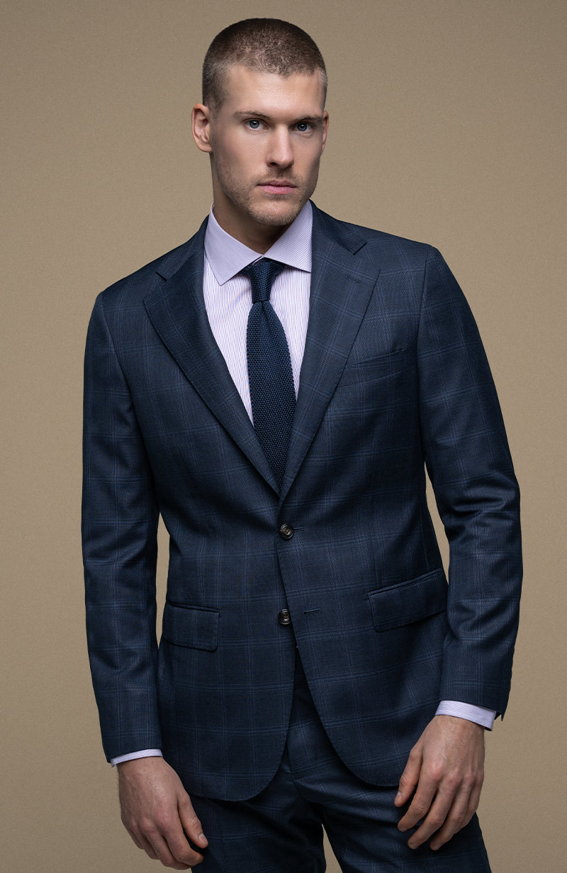 Man wearing a navy suit with a white shirt and dark tie on a beige background