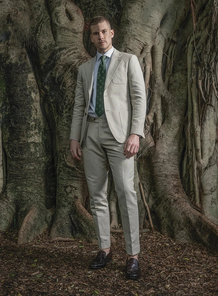 Man in a light gray suit standing in front of large trees