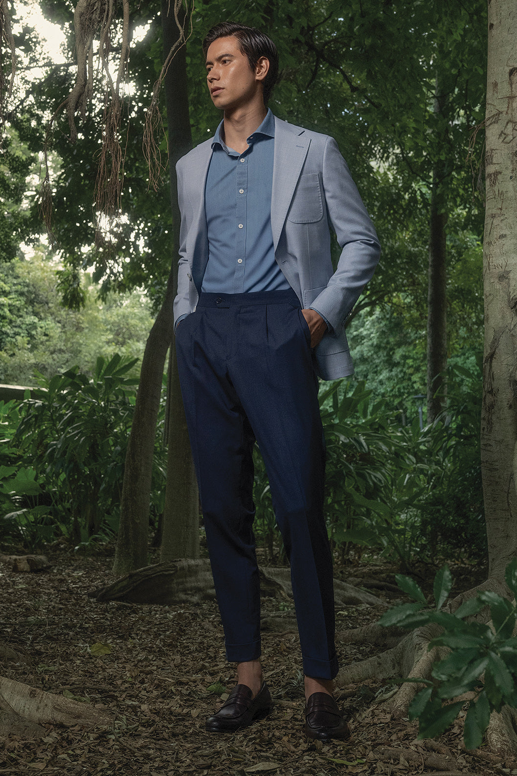 Man in a light gray blazer and blue shirt standing in a forest setting