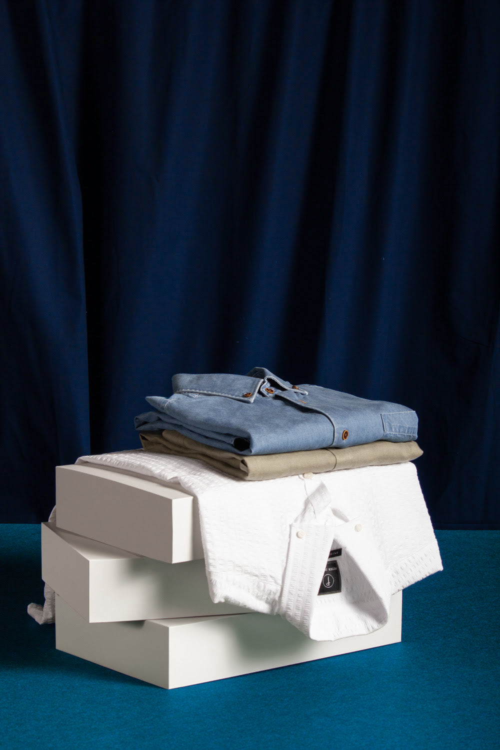 Stack of folded clothes on a white box against a dark blue curtain