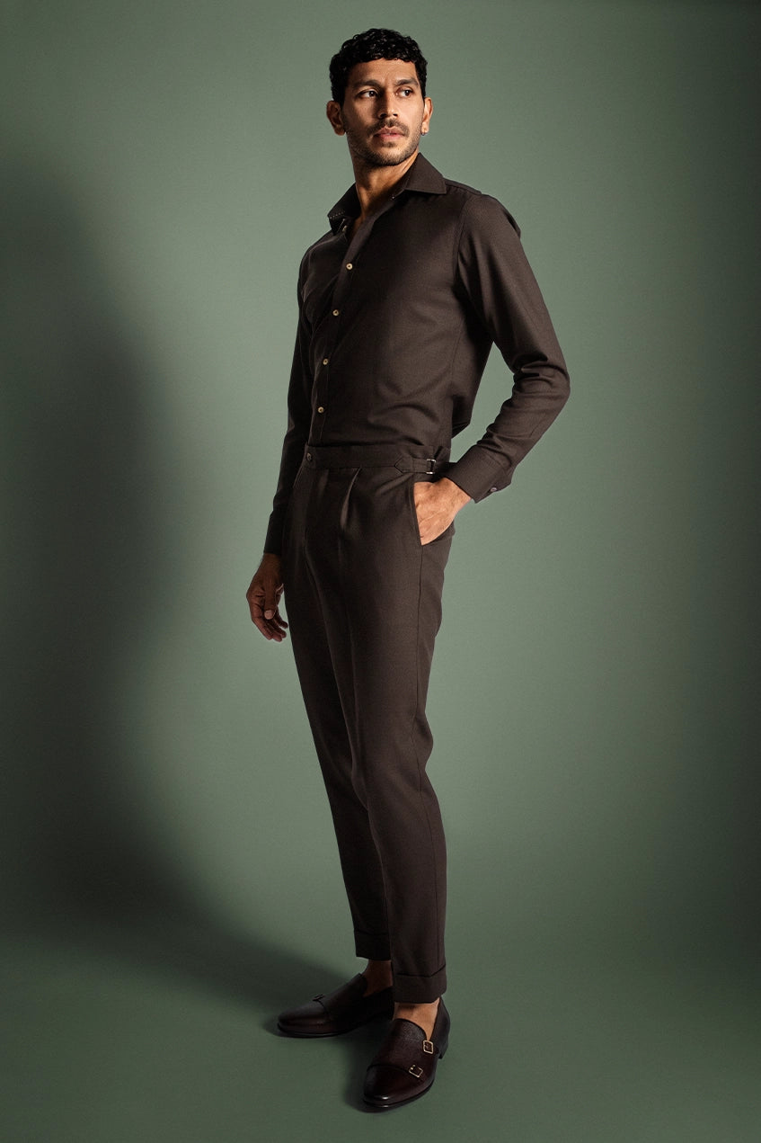 Man wearing a brown shirt and pants against a green background