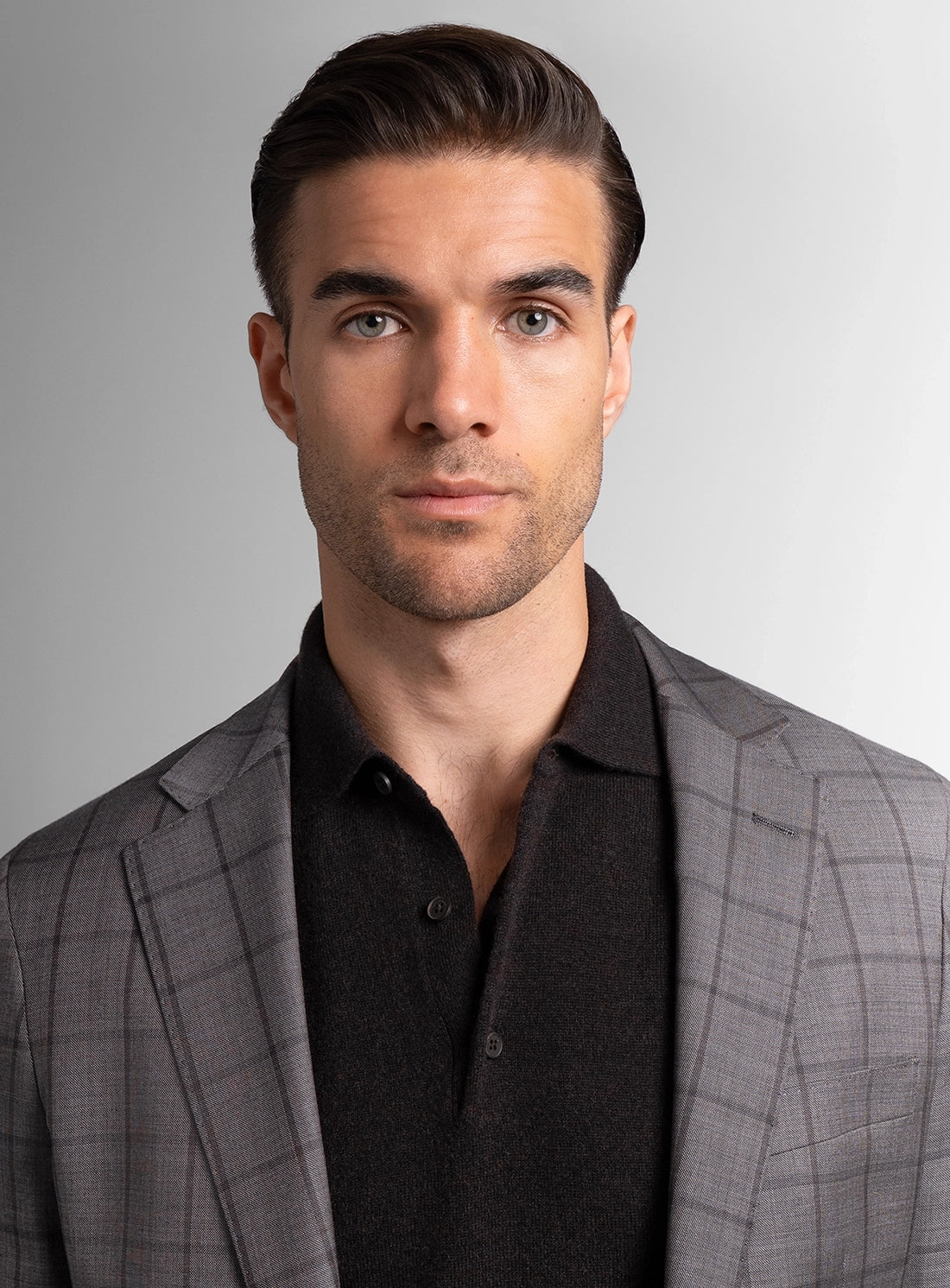 Man wearing a gray checkered suit jacket over a black shirt on a gray background
