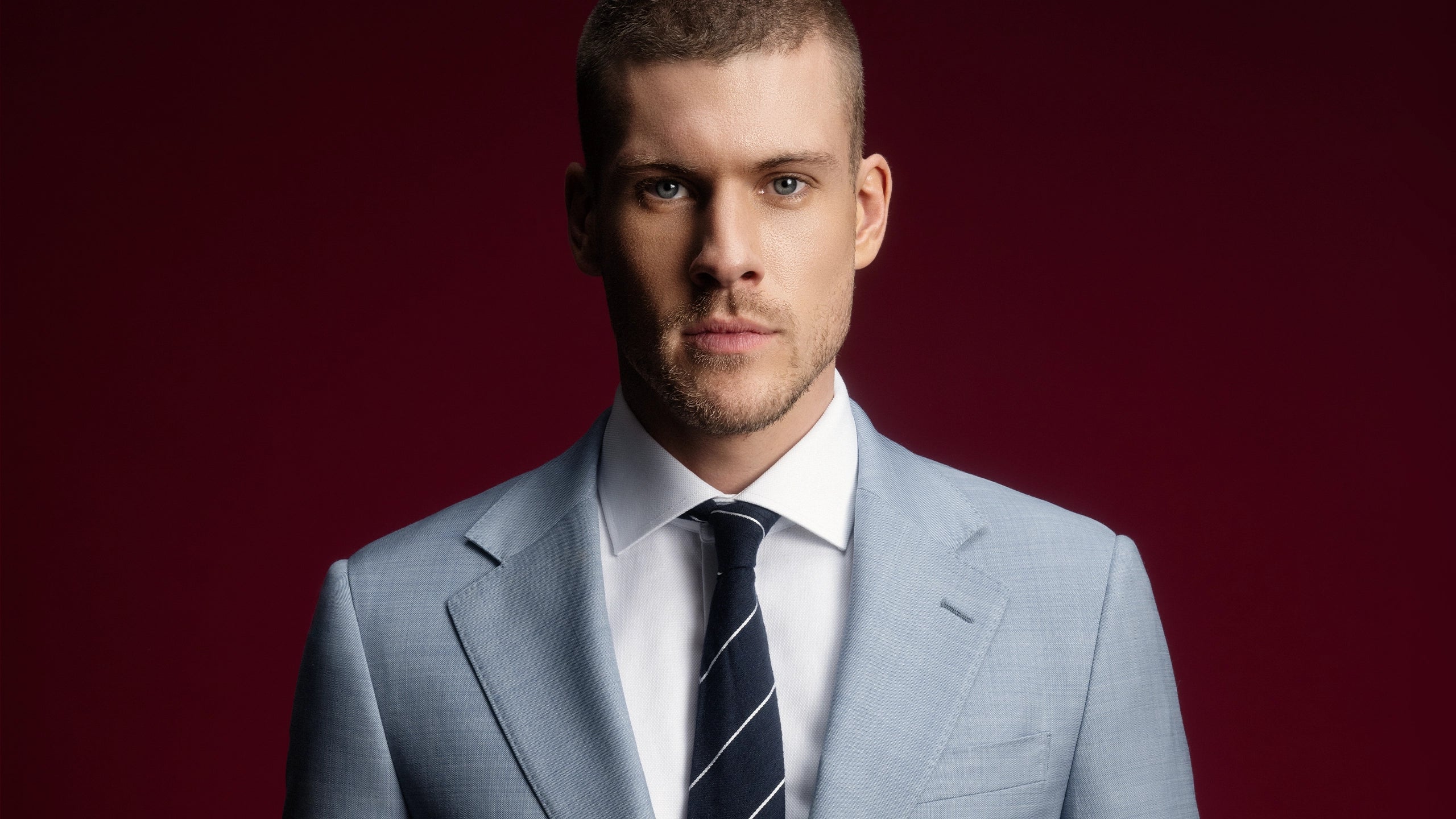 Man wearing a light gray suit with a striped tie against a red background