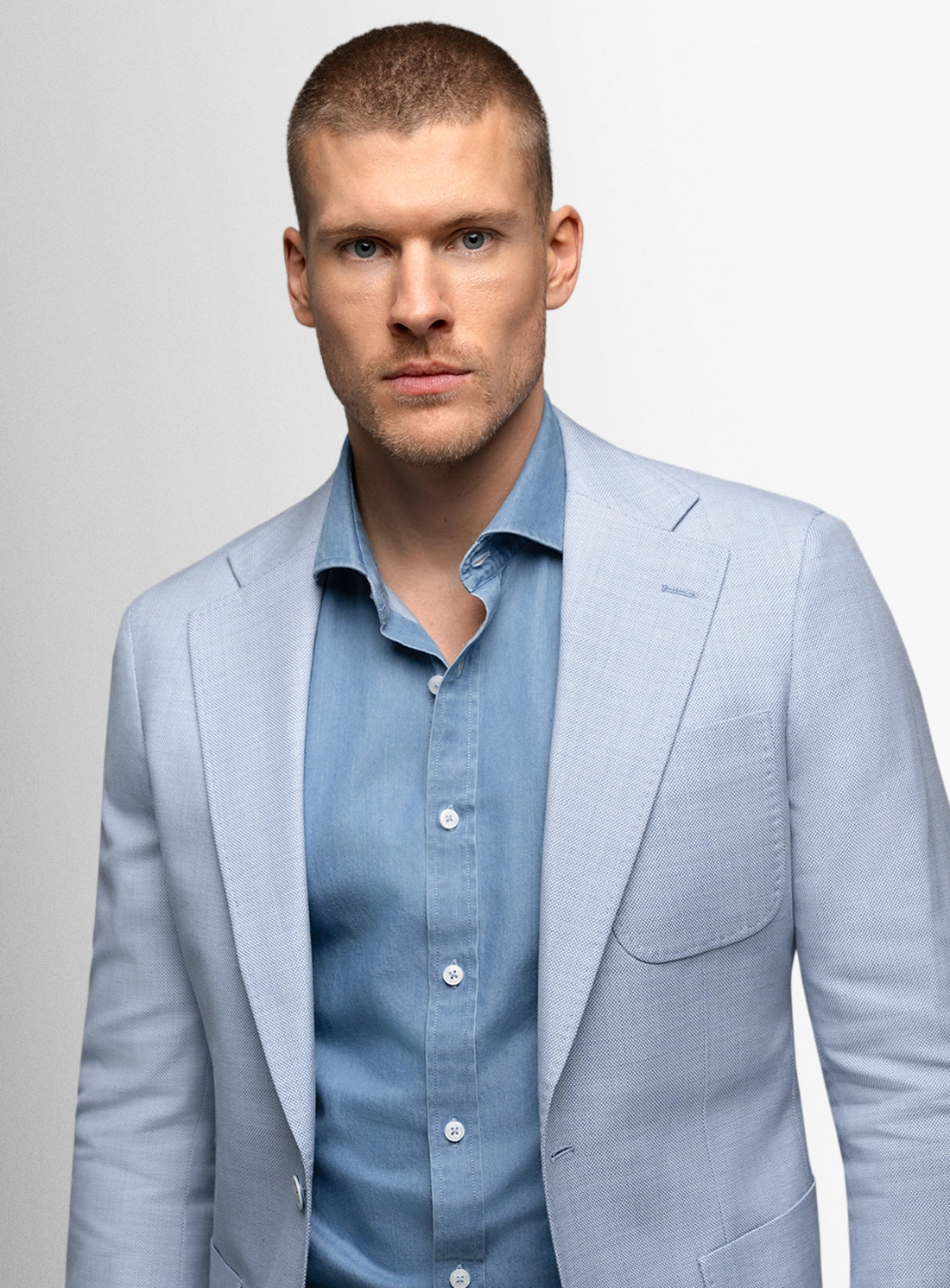 Man wearing a light blue suit and shirt against a plain background