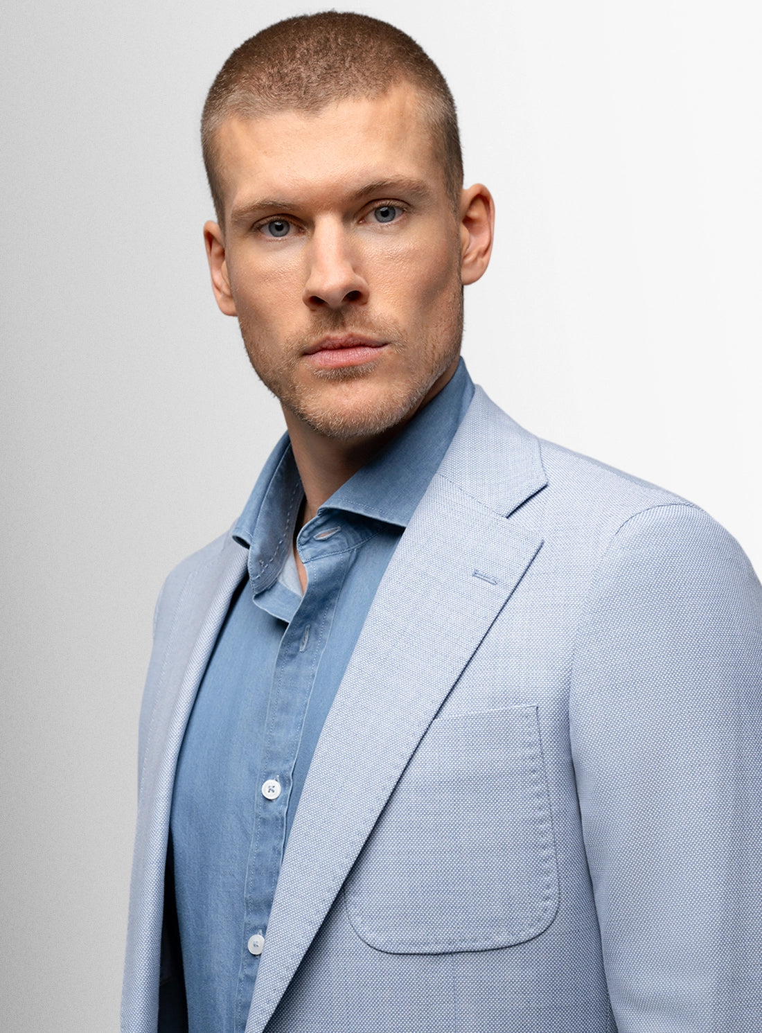 Man wearing a light blue suit jacket over a shirt against a plain background
