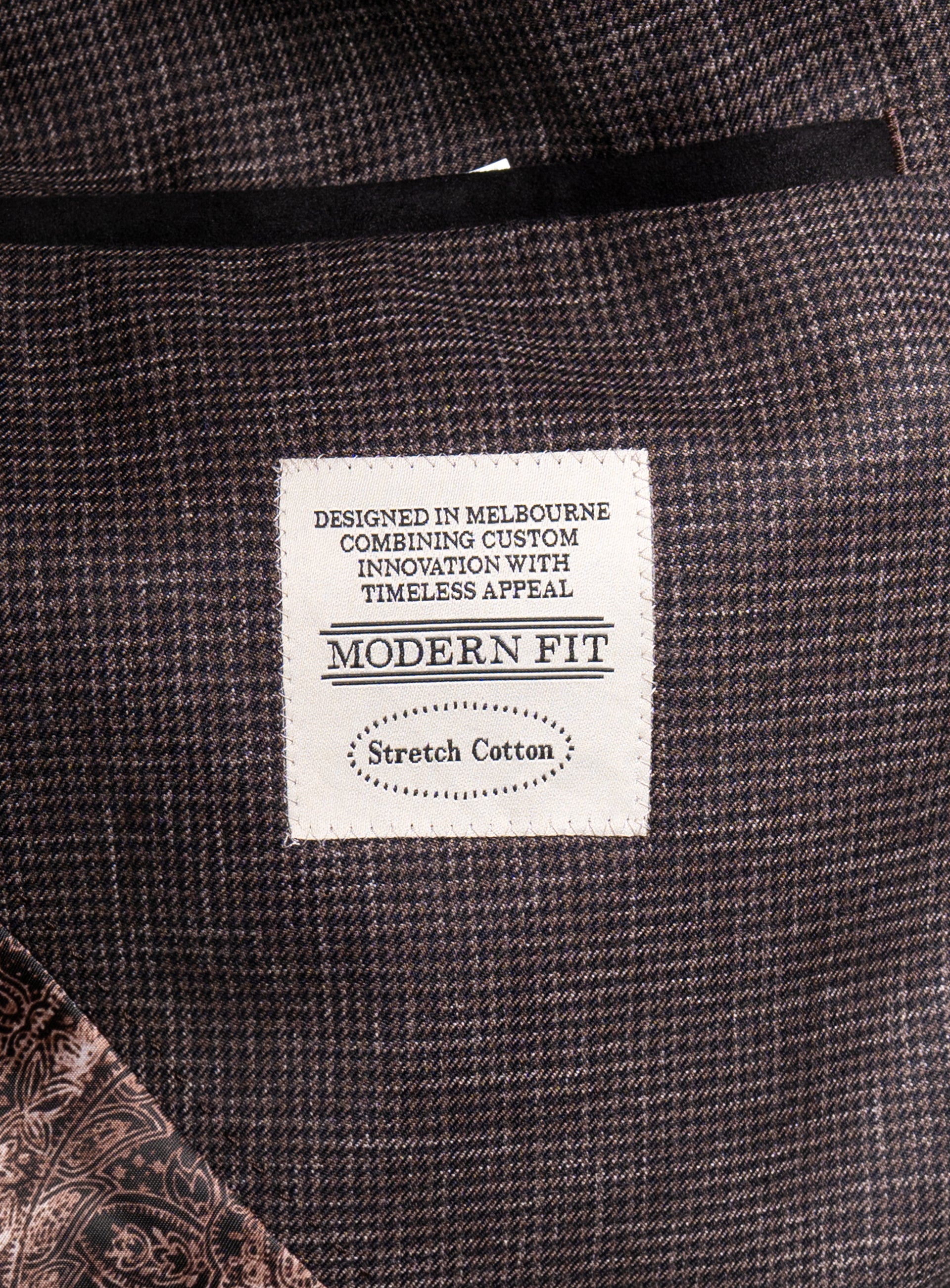 A label on the Mondovi Puppytooth Brown Jacket that says "Designed in Melbourne Combining Custom Innovations With Timeless Appeal - Modern Fit - Stretch Cotton"