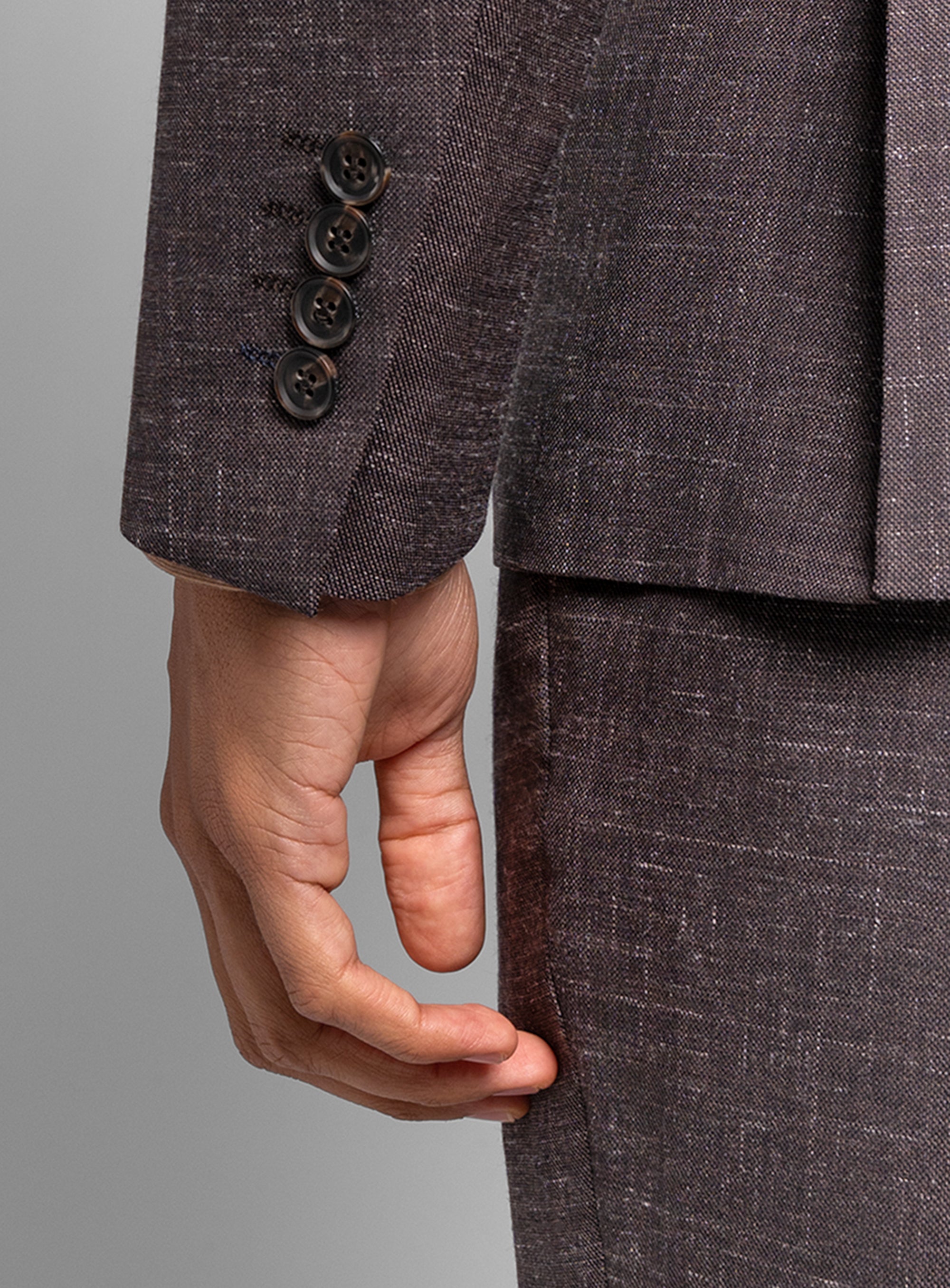 Close-up of a hand with a brown suit jacket with buttons on a gray background