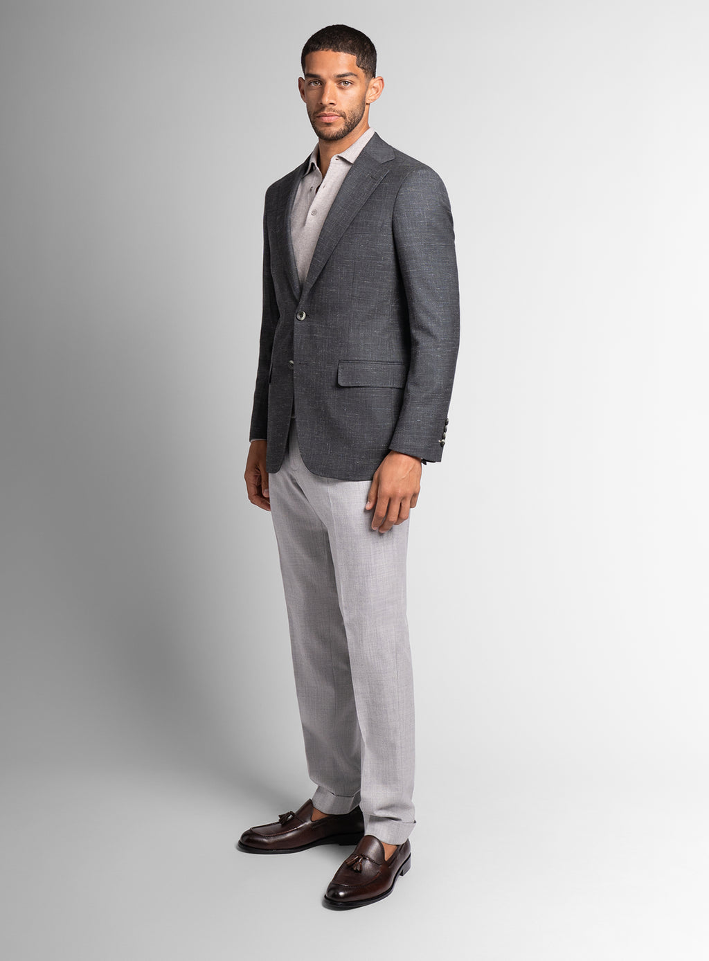 Man wearing a gray blazer, light gray pants, and brown shoes on a white background
