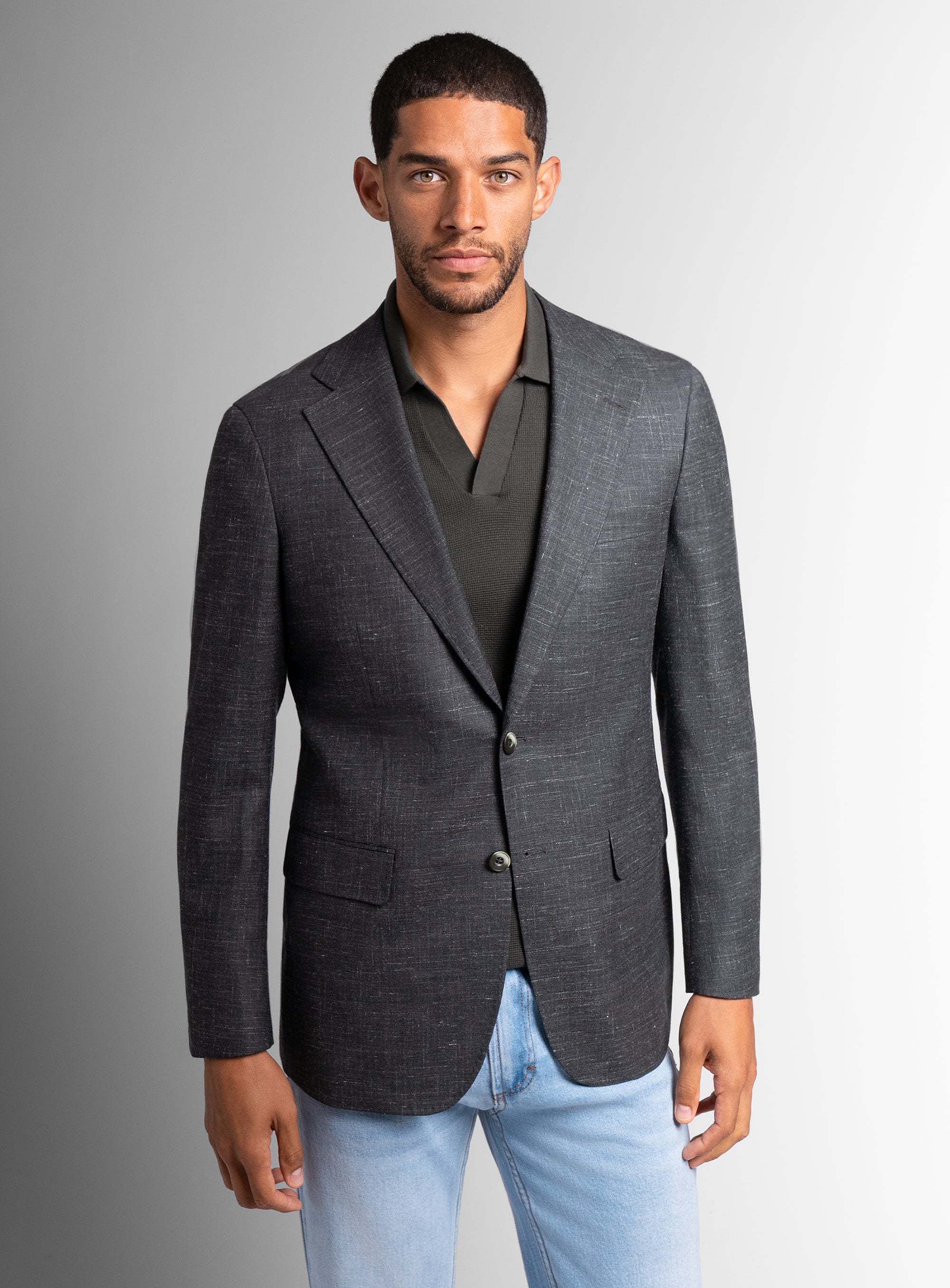 Man wearing a gray blazer over a black shirt with light blue jeans on a gray background