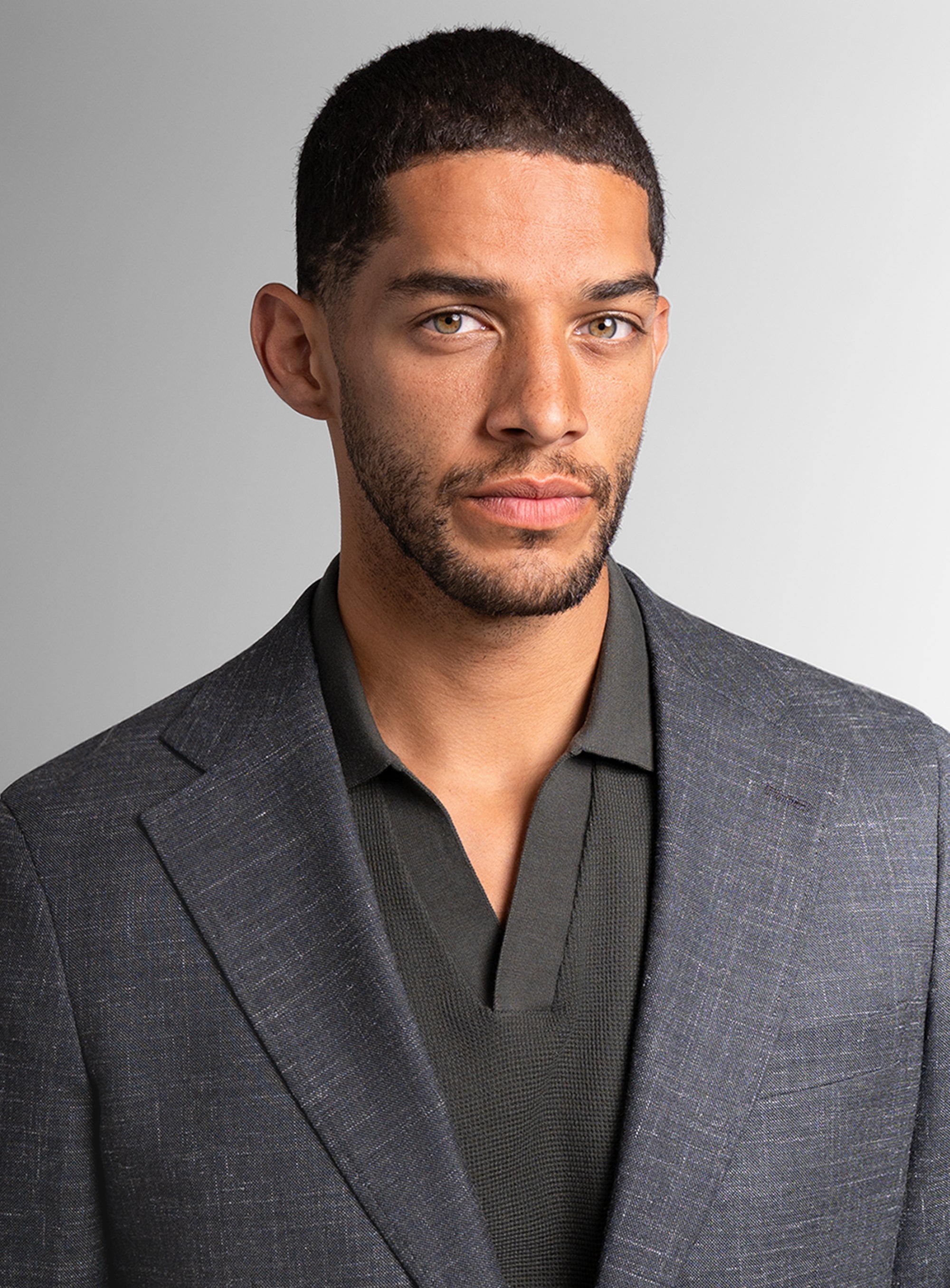 Man wearing a gray suit jacket over a dark green shirt against a gray background