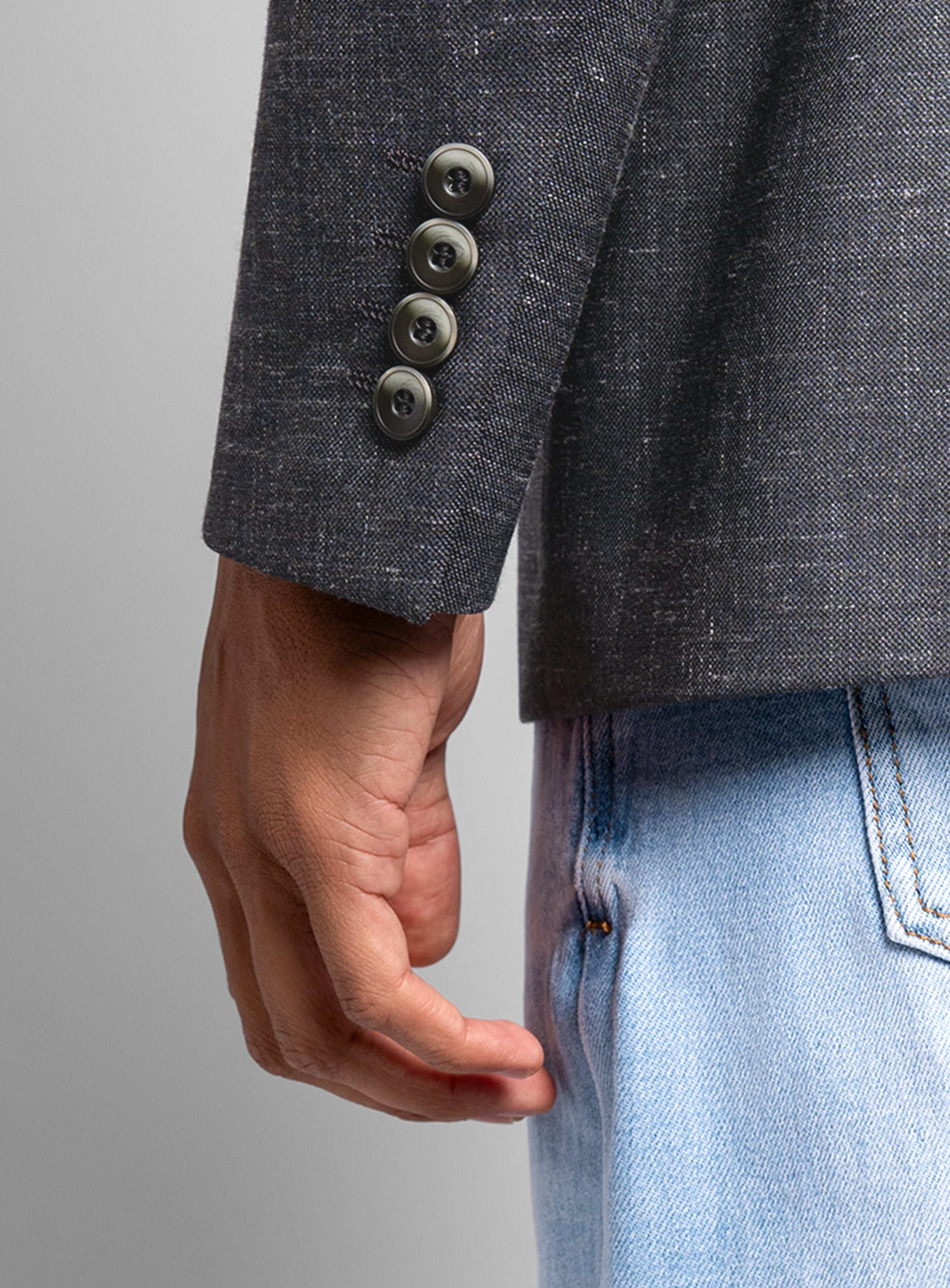 Close-up of a person wearing a dark gray blazer with three buttons on a light gray background.