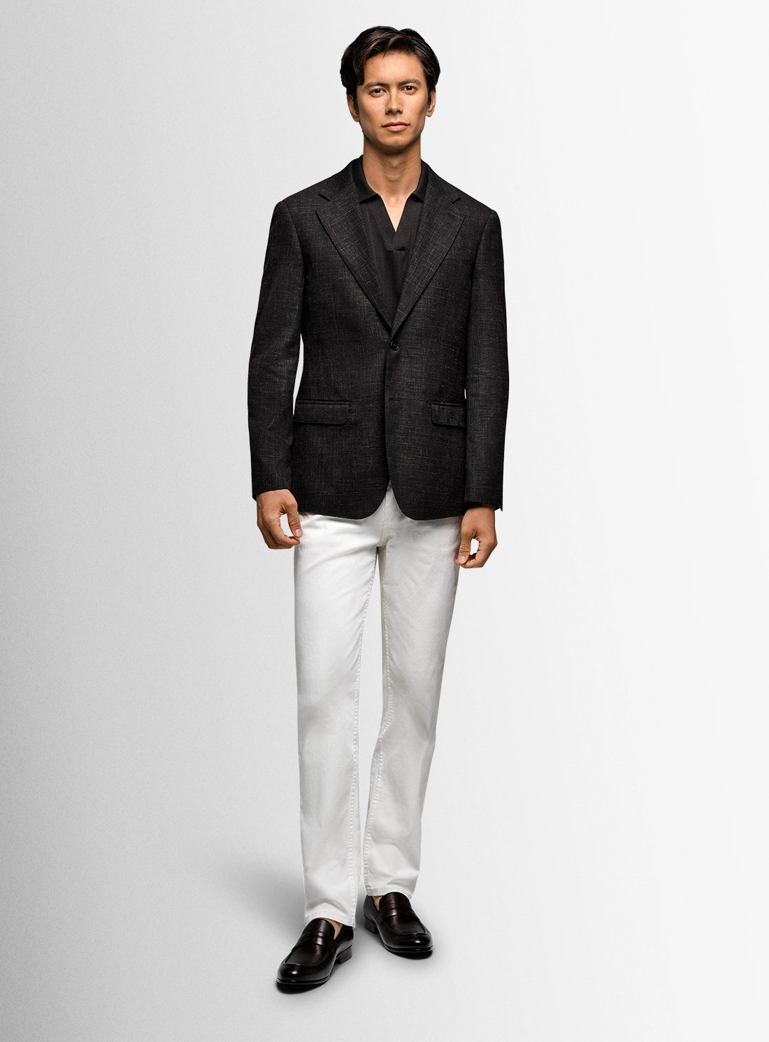 Man wearing a black blazer, white pants, and black shoes on a light gray background