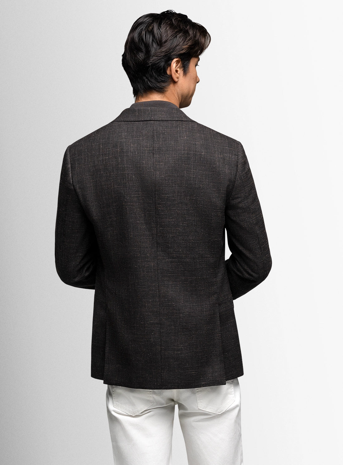 Man wearing a dark gray blazer and white pants on a light gray background