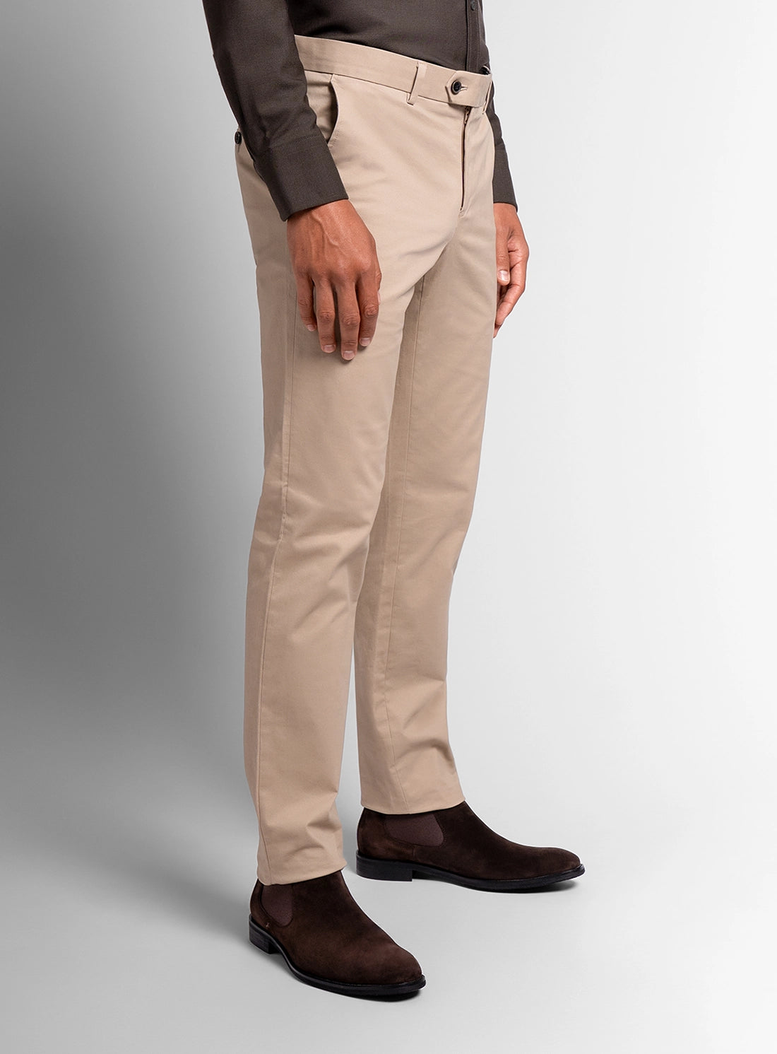Person wearing beige pants and brown shoes on a plain background