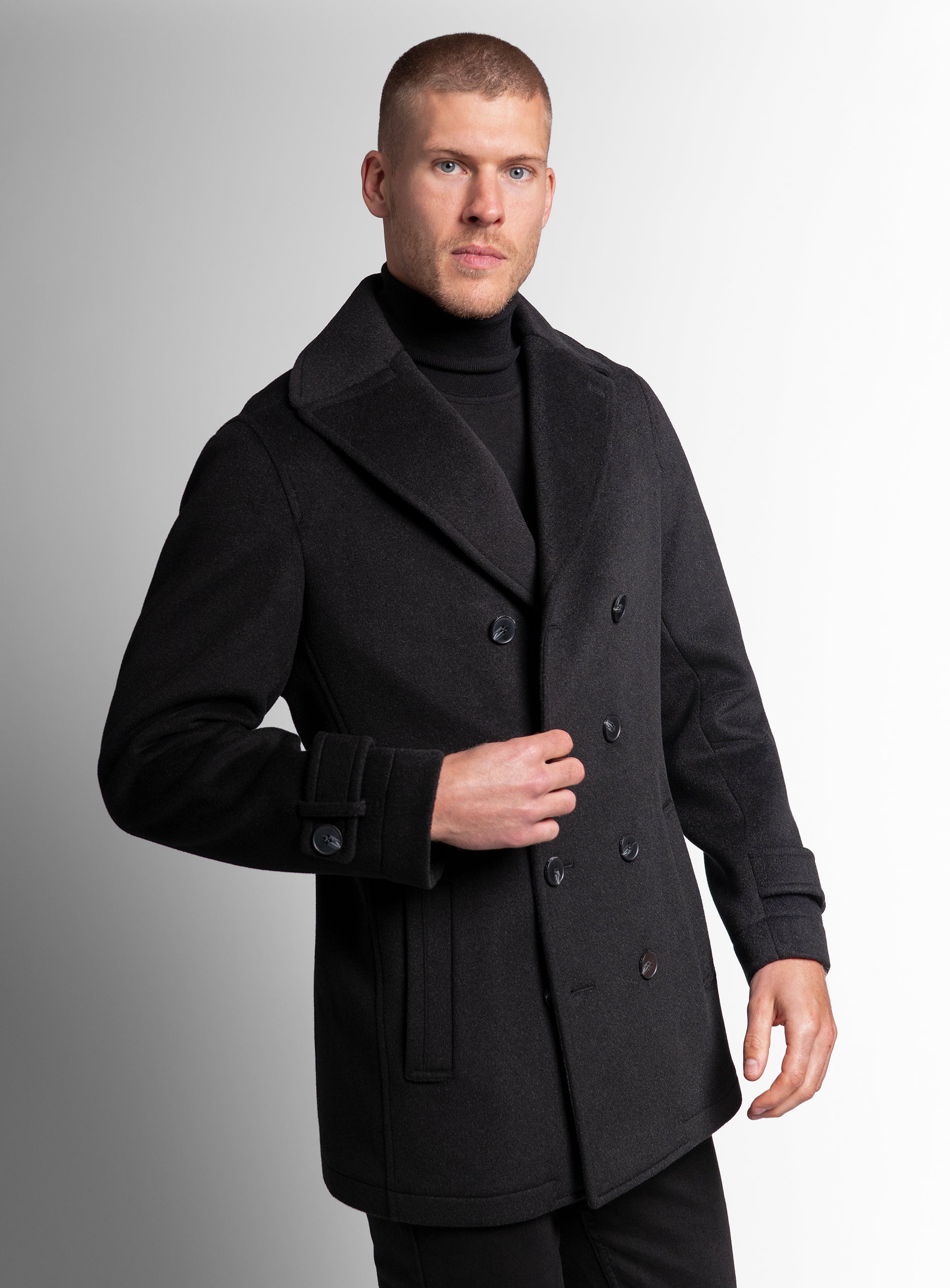 A man wearing the Bridge Black Peacoat, while holding one of the buttons