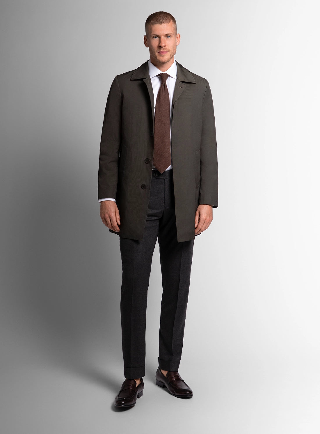 Man wearing a dark suit with a brown tie on a gray background