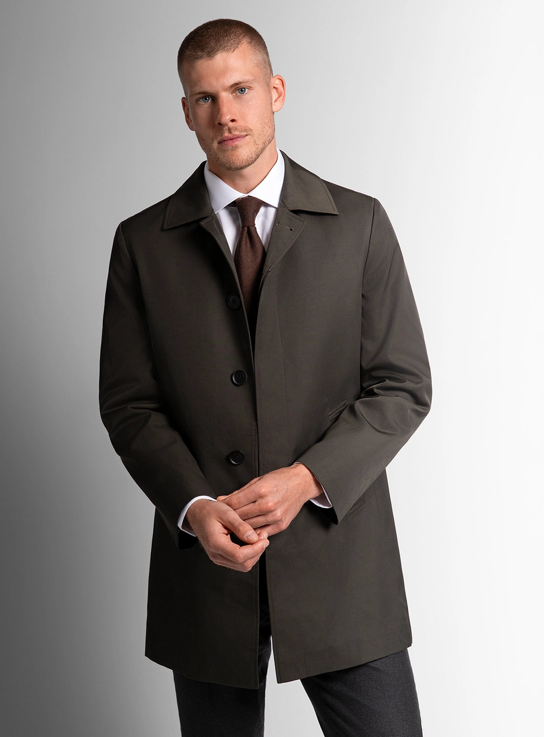 Man wearing a dark gray overcoat with a white shirt and brown tie on a gray background