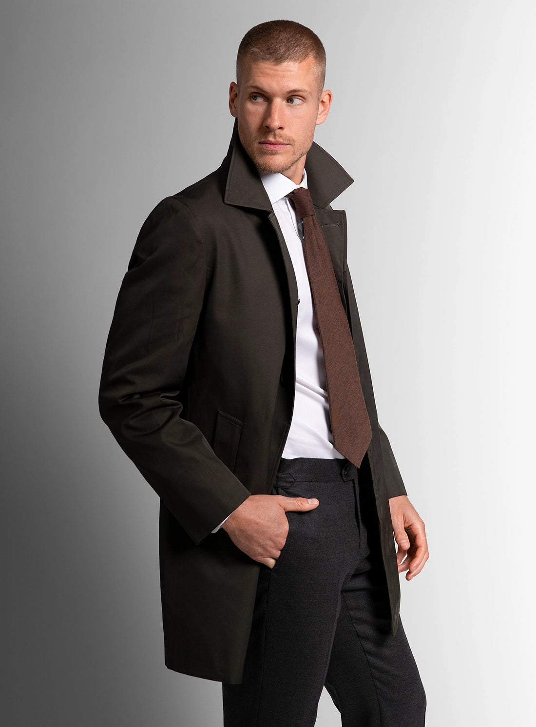 Man wearing a dark coat and tie against a gray background
