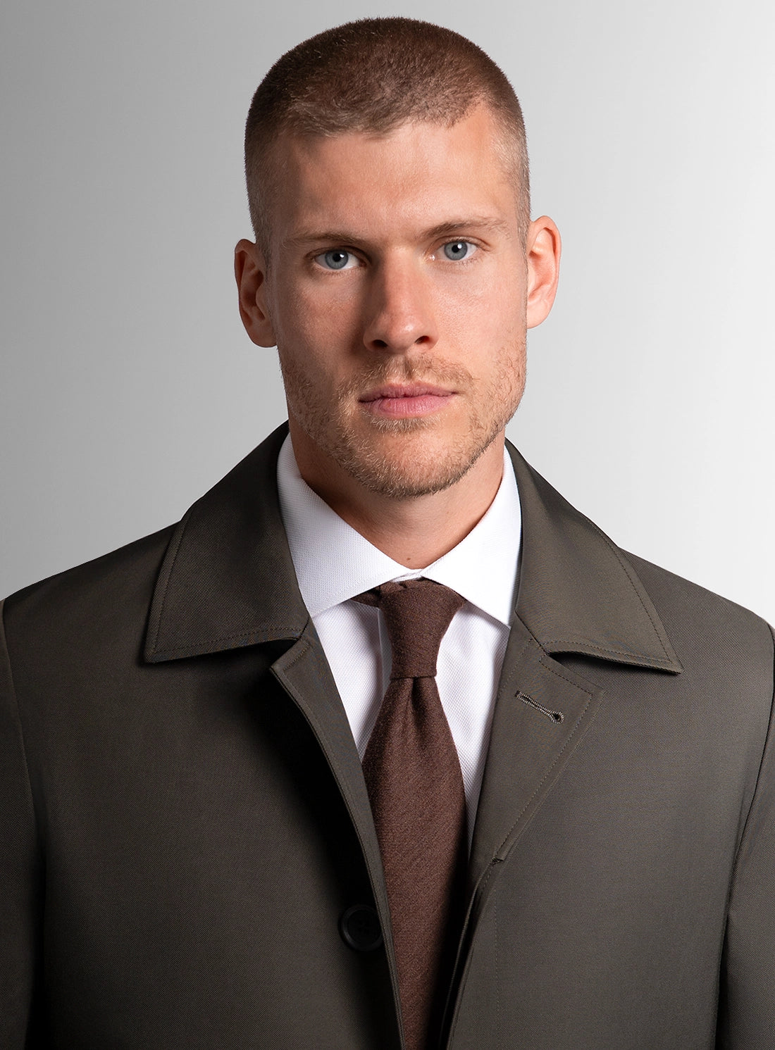 Man wearing a brown coat and tie against a gray background