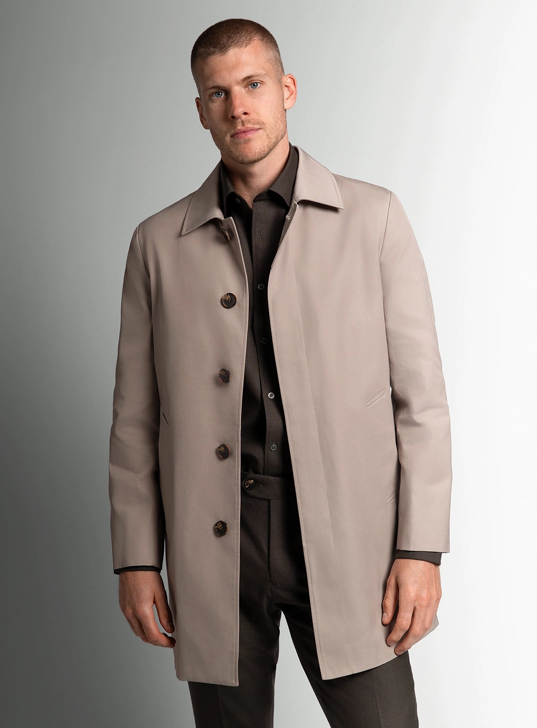 Man wearing a beige overcoat against a gray background