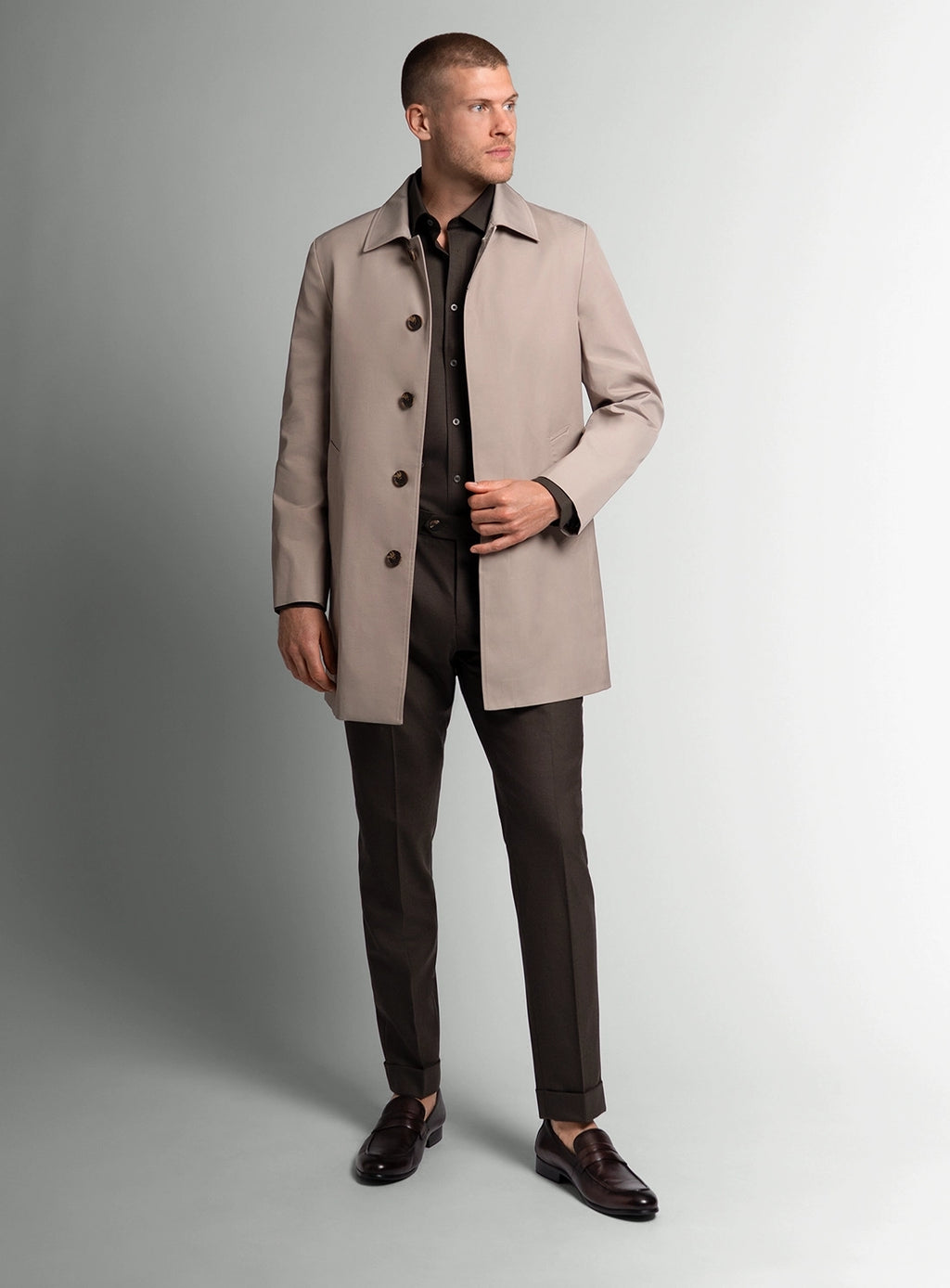 Man wearing a beige overcoat over a dark suit on a gray background