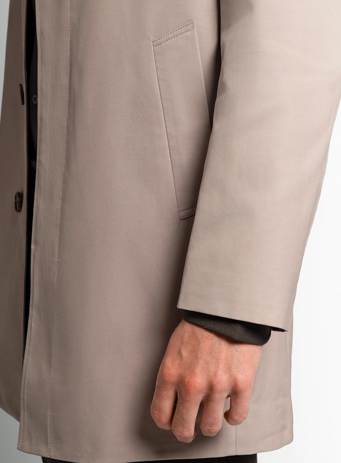 Close-up of a beige coat with a hand wearing a black glove peeking out from underneath.