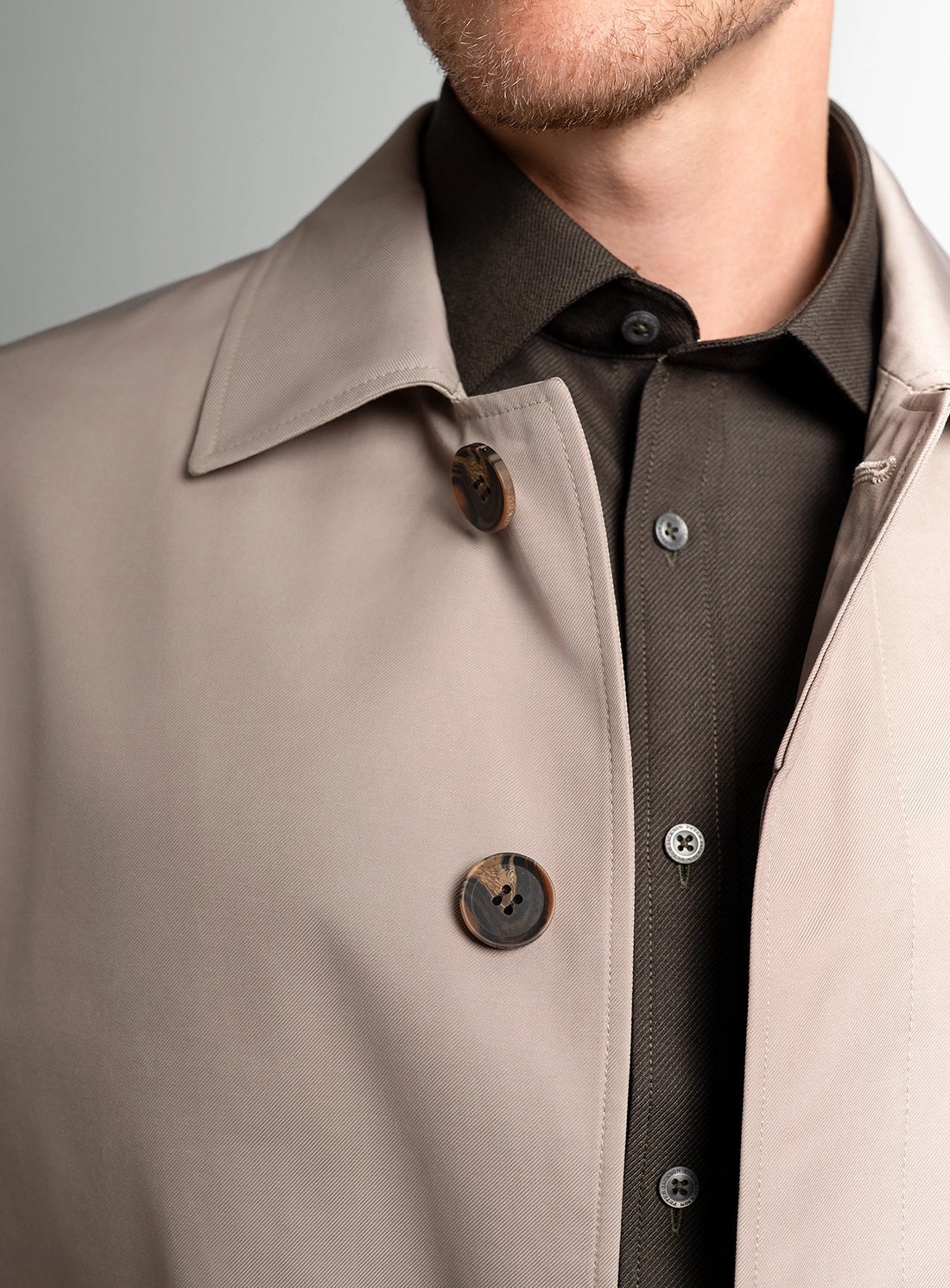 Close-up of a beige coat with a black shirt underneath on a gray background