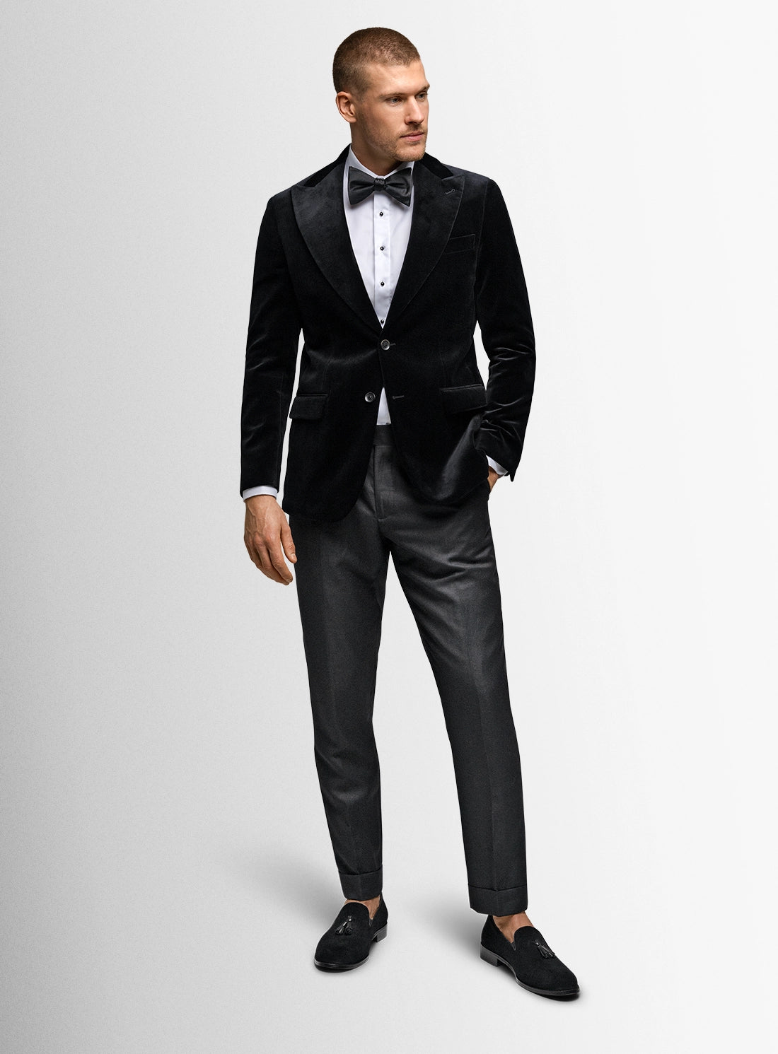Man wearing a black velvet tuxedo with a white shirt and black bow tie on a light gray background.