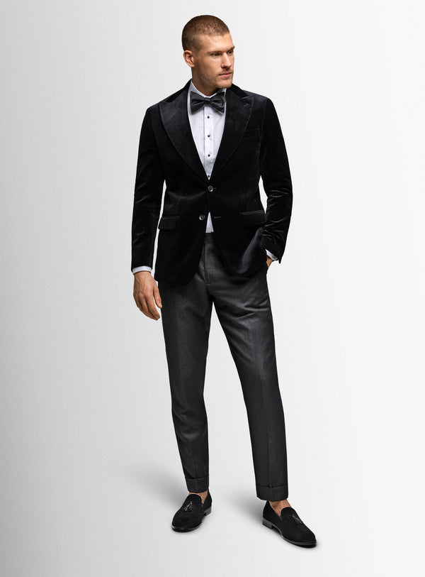Man wearing a black velvet tuxedo with a white shirt and black bow tie on a light gray background.
