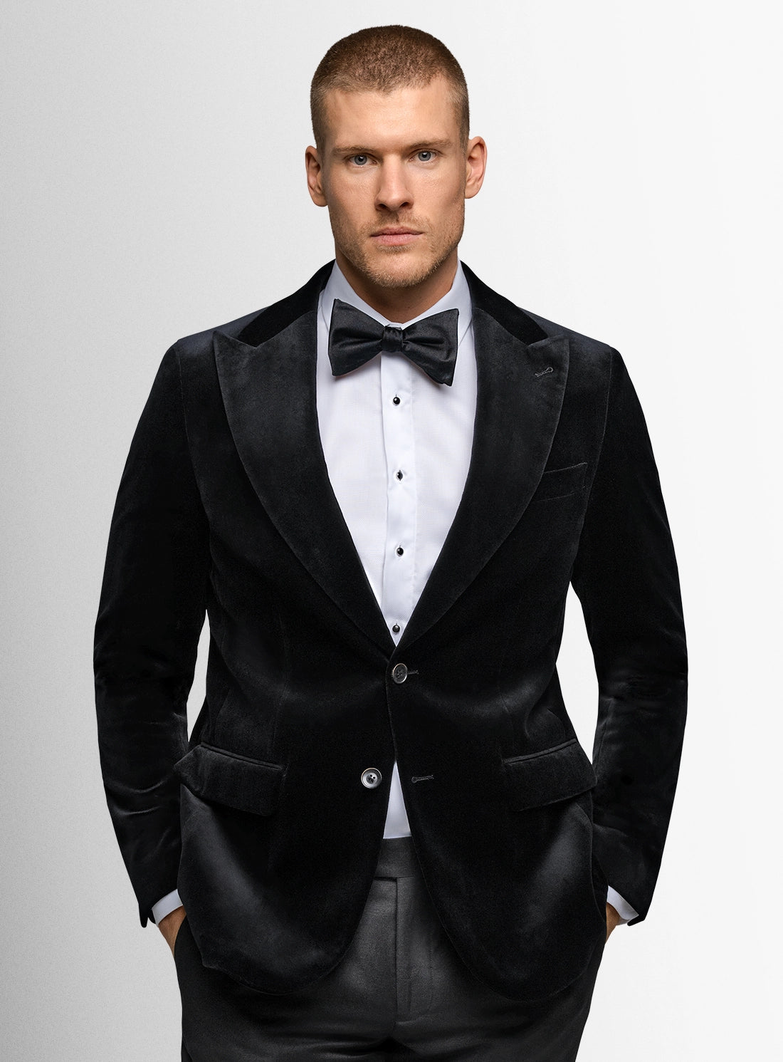Man wearing a black tuxedo with a white shirt and black bow tie on a gray background