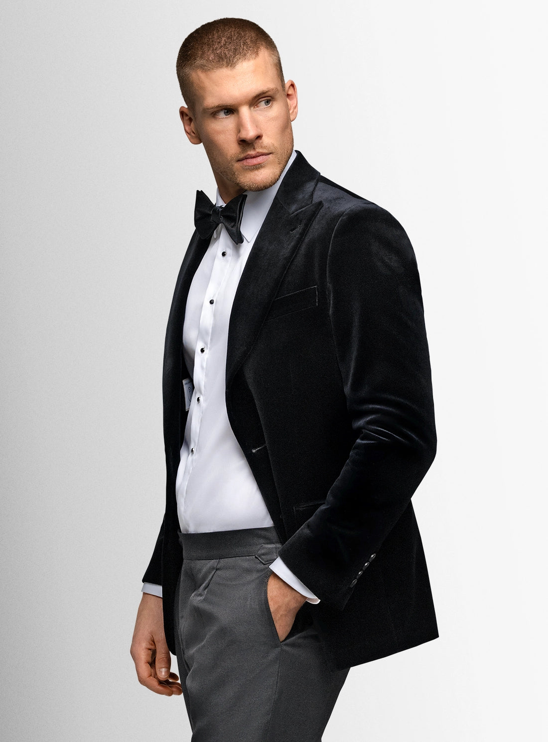 Man wearing a black tuxedo with a white shirt and gray pants on a light gray background