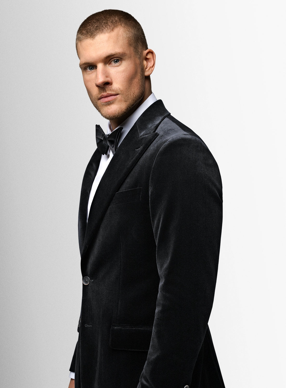 Man wearing a black tuxedo with a bow tie on a light gray background