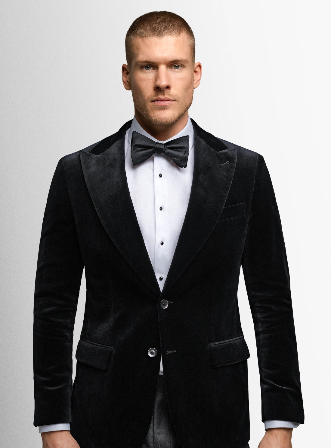 Man wearing a black velvet tuxedo with a bow tie on a gray background