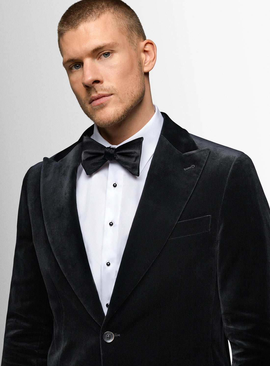 Man wearing a black tuxedo with a bow tie against a gray background
