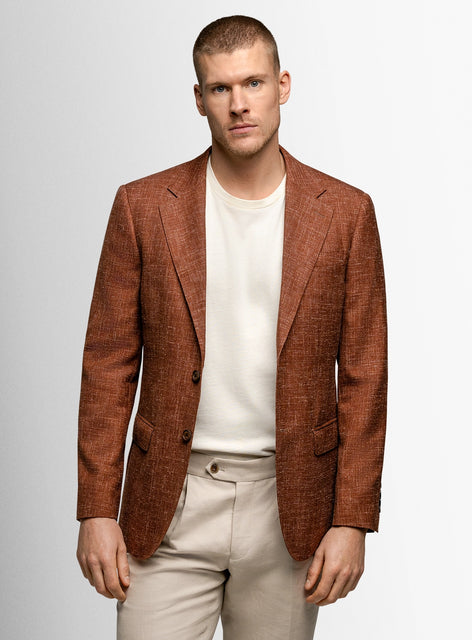 Man wearing a brown blazer over a white shirt and beige pants on a light gray background
